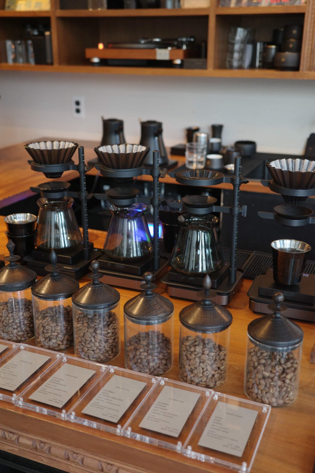 Coffee bar counter lined with pour-over stands, glass carafes, and jars of beans with printed tasting cards.