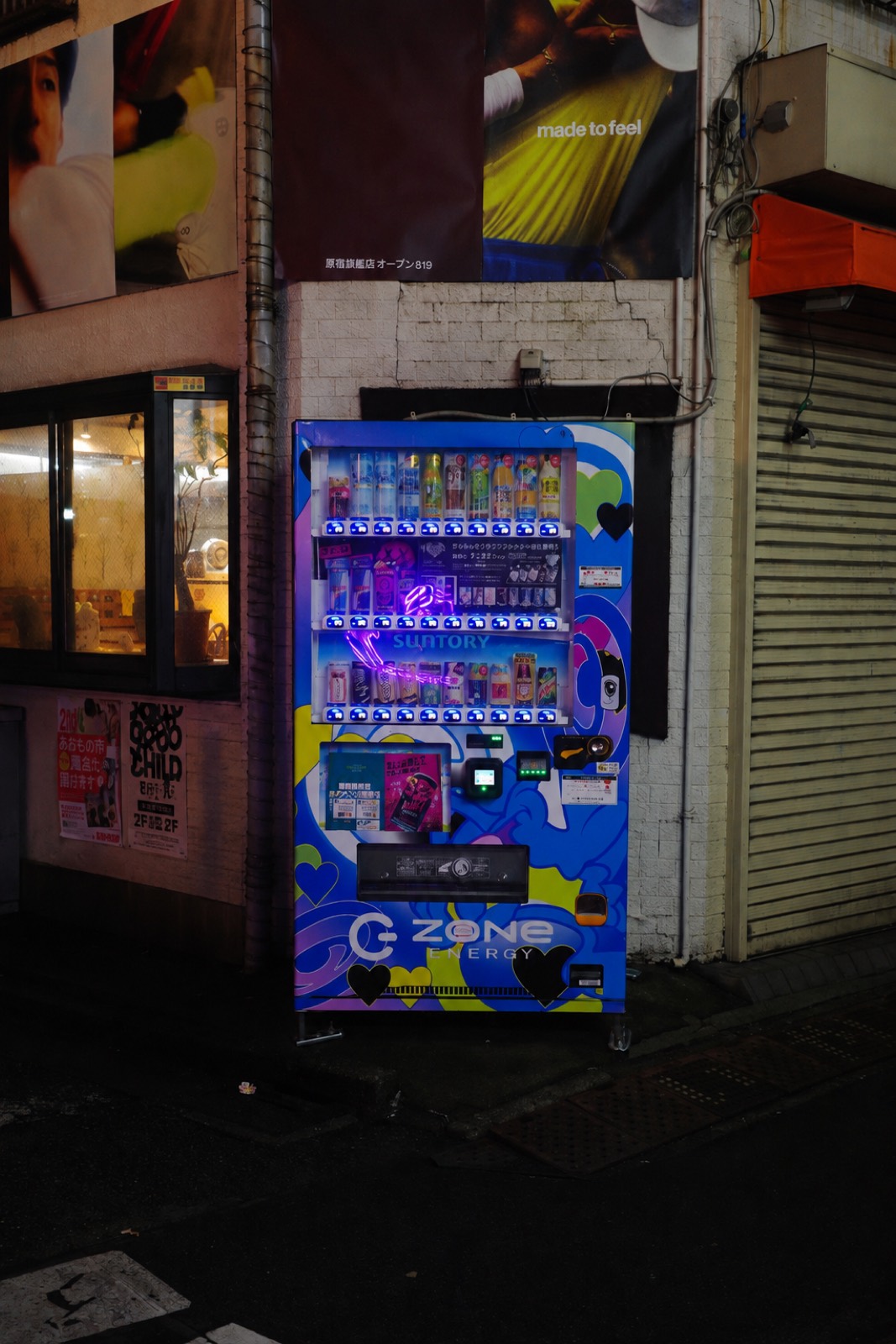 Brightly wrapped energy-drink vending machine glowing blue and violet on a dark backstreet, beside a shuttered storefront.